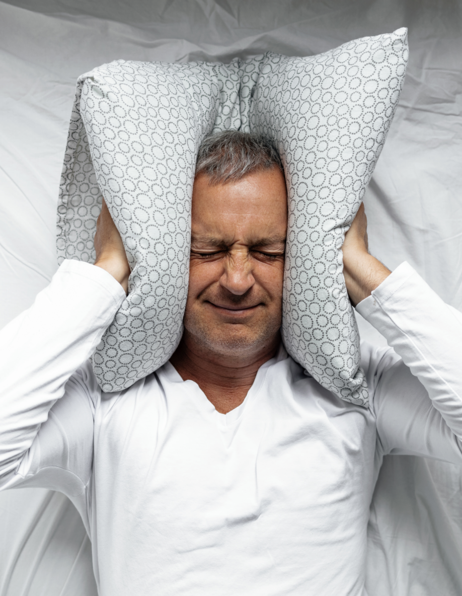 Mann drückt sich Kissen auf die Ohren wegen störender Ohrgeräusche.